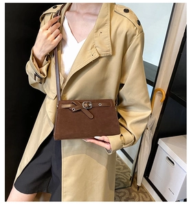 Brown frosted suede crossbody bag with decorative strap buckle on a beige coat