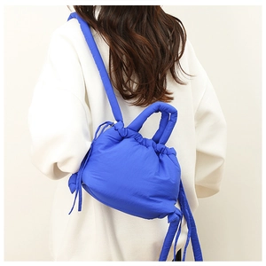 Detail of blue quilted down backpack with drawstrings worn by a model in a minimal setting