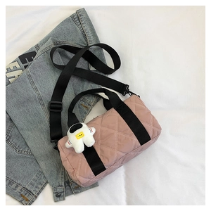 Pink quilted nylon barrel bag with astronaut plush charm on casual denim background