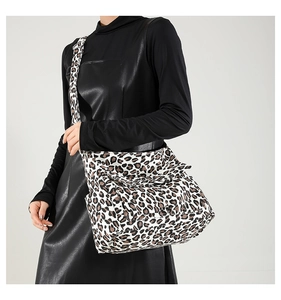 Leopard print crossbody bag with wide strap worn over a black dress in a studio