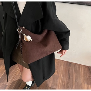 Détail d'un sac hobo en daim marron foncé avec un charme sportif et une bandoulière en cuir