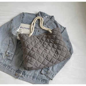Gray quilted tote bag with white rope handles displayed on a blue denim jacket