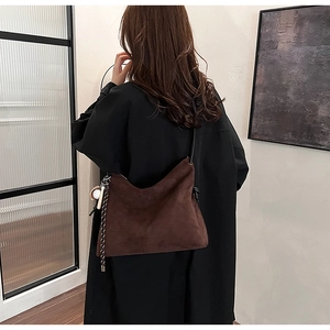 Détail d'un sac bandoulière en daim marron avec pompon porté par un mannequin dans un salon