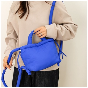 Blue puffer nylon shoulder bag shown with knotted detail on a model in urban style