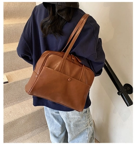 Caramel brown PU leather tote bag with front pocket shown on shoulder of a model