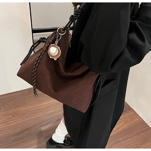 Détail du grand sac hobo en daim marron avec bandoulière nouée et breloque baseball
