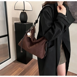Détail du sac hobo en daim marron foncé avec bandoulière nouée et pendentif baseball