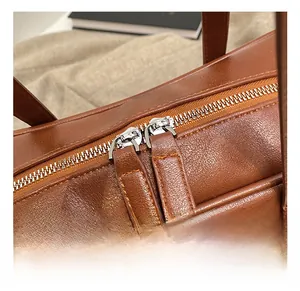 Detailed close-up of dual silver metal zippers on caramel brown lychee texture leather bag