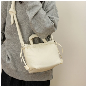Detail view of cream quilted nylon crossbody bag with drawstring side and knotted strap