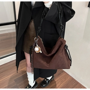Détail du sac à bandoulière en daim marron foncé avec sangle nouée et breloque baseball