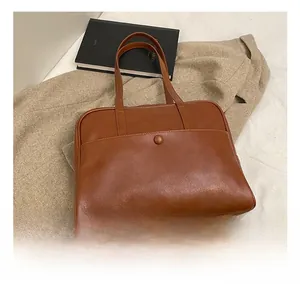 Detail view of brown PU leather shoulder bag featuring functional snap button front pocket