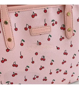 Détail d'un sac rose avec imprimé cerise, cuir grainé et rivets dorés sur la sangle
