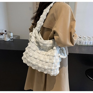 Chic sac à bandoulière blanc tissé porté avec un trench-coat dans un café chaleureux