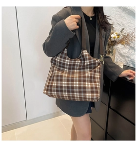 Close-up of a brown plaid canvas tote bag with adjustable wide strap and gold hardware detail