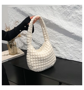 Detail of a beige quilted puffer shoulder bag featuring soft textured fabric and a padded handle