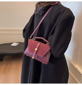 Detail of burgundy faux leather and suede crossbody bag styled with a black autumn coat