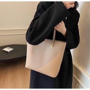 Detail of a beige pebbled leather tote bag with thin shoulder strap and gold hardware