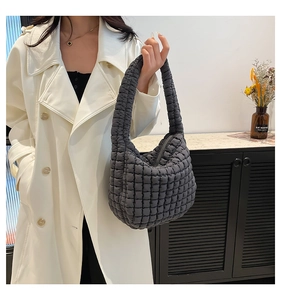 Detail of a dark grey quilted hobo bag shown by a model in a minimalist setting