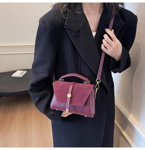 Detail view of burgundy suede patchwork handbag worn with a black autumn coat