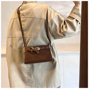 Close-up of a brown faux suede crossbody bag featuring a leather strap detail on a model