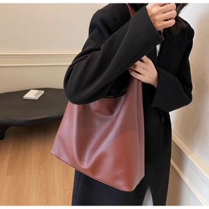 Detail of soft brick red lychee grain leather tote bag worn with a black coat