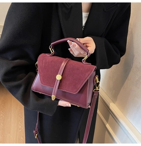 Detail view of burgundy faux suede shoulder bag with gold hardware on a black coat