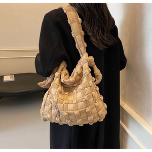 Sac à bandoulière matelassé beige porté sur un manteau noir élégant d'hiver