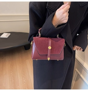 Close-up of burgundy suede and leather handbag with gold buckle and structured handle