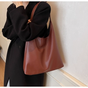 Detail of a dark brown pebble leather hobo bag worn with a black wool coat for autumn