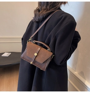 Detail of a brown suede and leather crossbody bag with golden hardware on a black coat