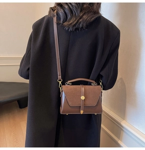 Detail of dark brown suede and leather crossbody bag featuring gold buckle on black coat