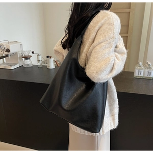 Close-up of black lychee-textured leather tote bag worn on shoulder in a modern café