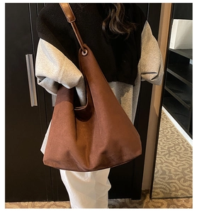 Détail d'un sac bandoulière en daim marron avec œillets métalliques et texture mate douce