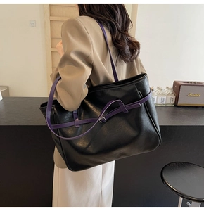 Detail of black pebbled leather tote bag featuring a vibrant purple shoulder strap and metal buckle