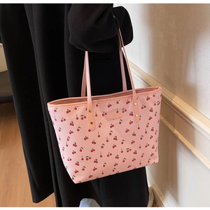Gros plan du sac cabas en similicuir rose avec motifs cerises rouges et plaque de marque