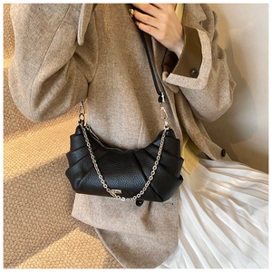 Detail of black pleated crescent shoulder bag with silver chain strap on model