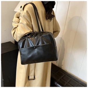 Close-up of matte black leather tote bag featuring a front pocket with round buckle