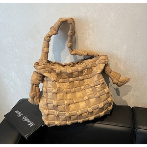 Sac à épaule matelassé kaki au design tressé texturé posé sur un siège en cuir noir