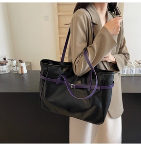 Detail of black leather tote bag with purple straps shown on a model in a cafe setting