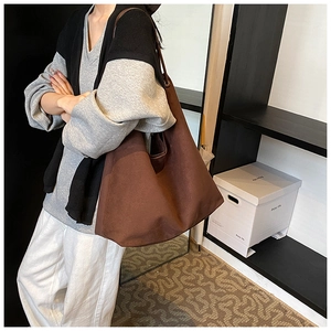 Vue latérale d'un grand sac fourre-tout en tissu marron porté par un mannequin en studio
