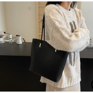 Detail of classic black tote bag with lychee texture and gold metal accents on strap