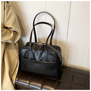 Detail view of the black PU leather tote bag with silver zippers on a luxury stool
