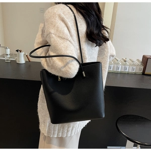 Detail of a black pebbled leather tote bag shown with slim straps and gold hardware
