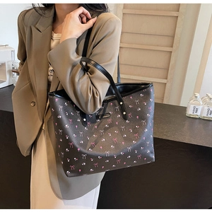 Détail de l'imprimé floral à nœuds sur un sac fourre-tout noir en similicuir à rivets