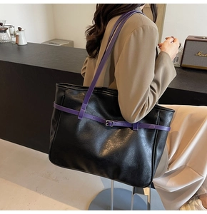 Detail of black faux leather tote with purple strap and silver buckle in a cafe setting