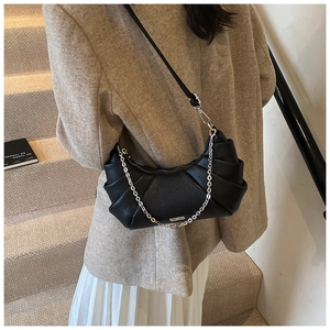 Close-up of black pleated PU shoulder bag with silver chain strap worn by a model