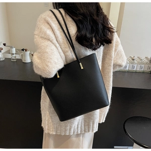 Detail of black pebbled leather tote bag with gold hardware on model in cozy cafe