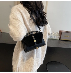 Detail of black crossbody bag with suede texture and gold round buckle on female model