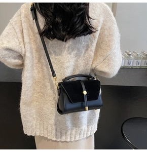 Chic black crossbody bag with mixed textures and gold buckle worn with a knit sweater