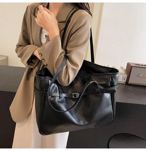 Detail view of black PU leather tote bag with silver buckle worn with a casual blazer